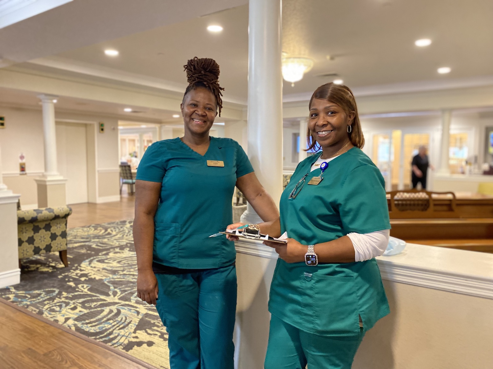 Two smiling Kingston Healthcare employees dressed in teal scrubs.