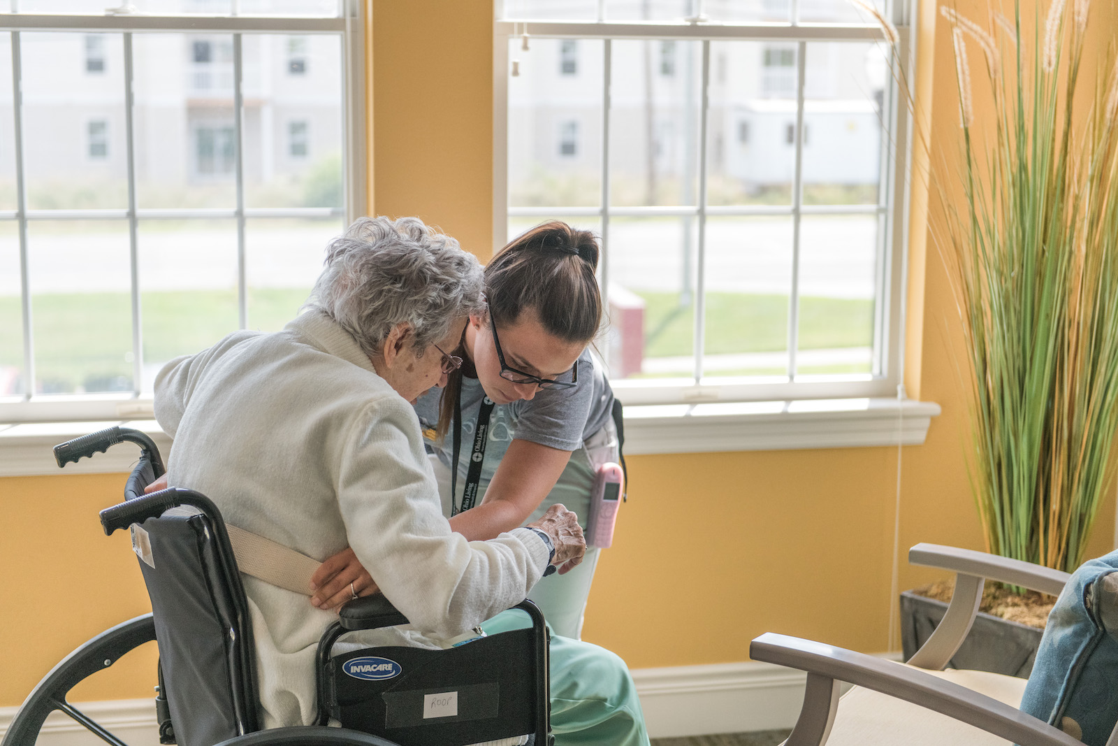 A Kingston Healthcare caregiver assists a senior resident in a wheelchair.
