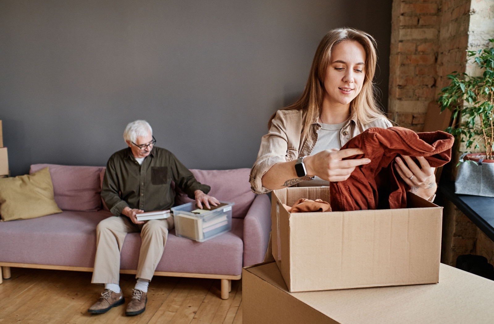 A young adult helping their older parent pack a box of clothes while preparing for a move to senior living.