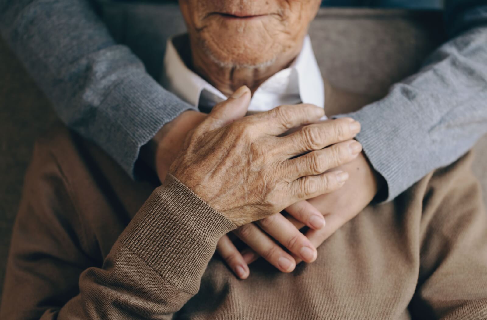 Close-up of a senior parent resting their hands over their child's placed on their chest.
