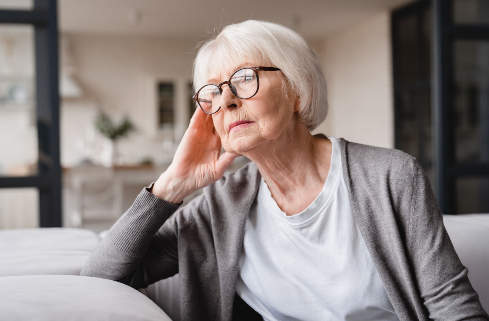 An older adult sitting on a couch in their home looking out the window.