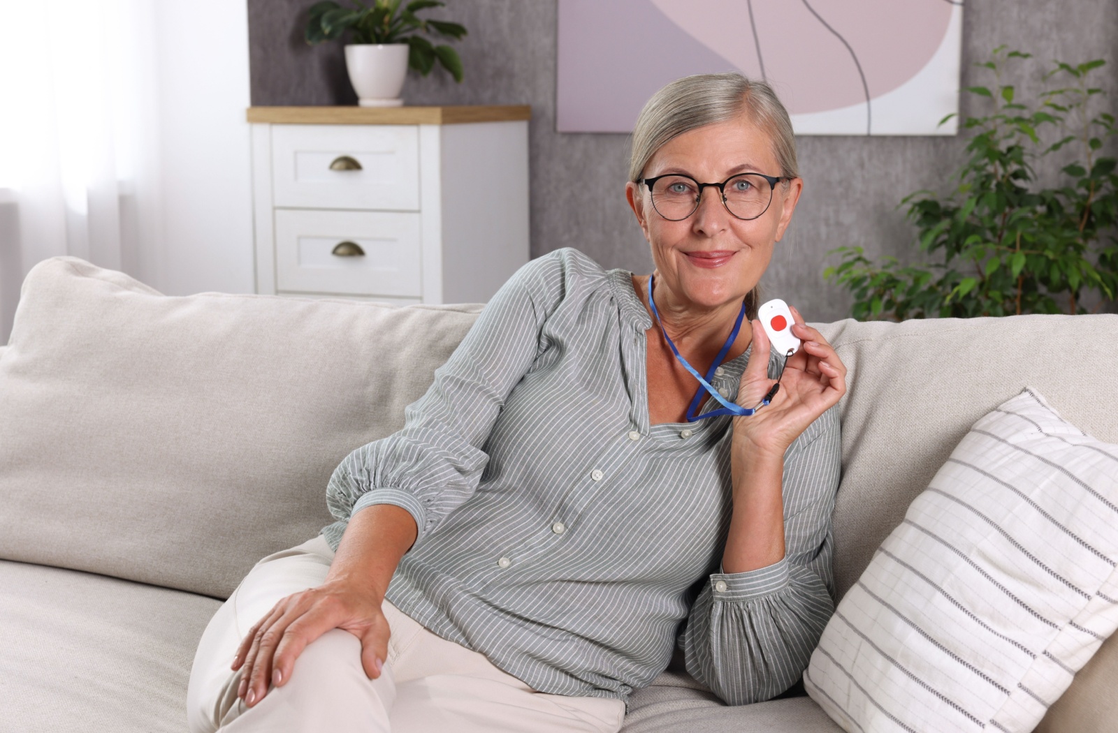 A smiling senior holds up their necklace with a call button, happy that help is a button press away.