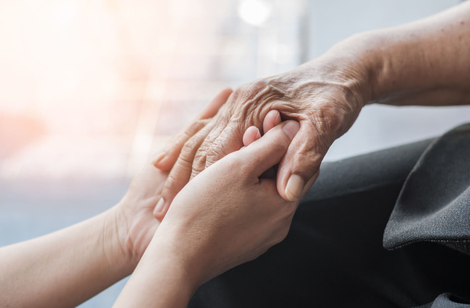 A close-up image of an older adult clasping the hand of their older parent to show support.