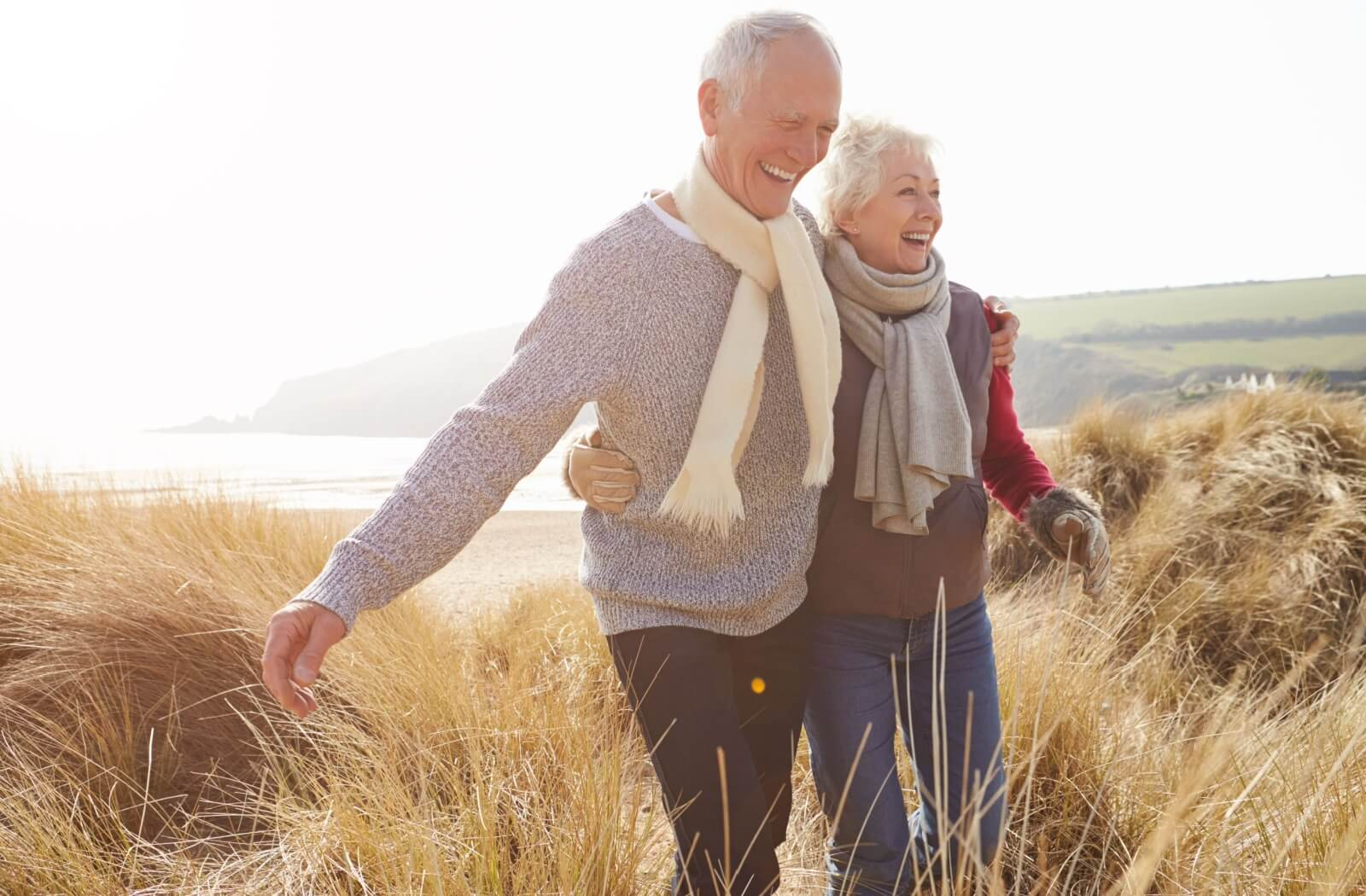 A senior couple walk through grasslands together while embracing, enjoying their connection and the outdoors