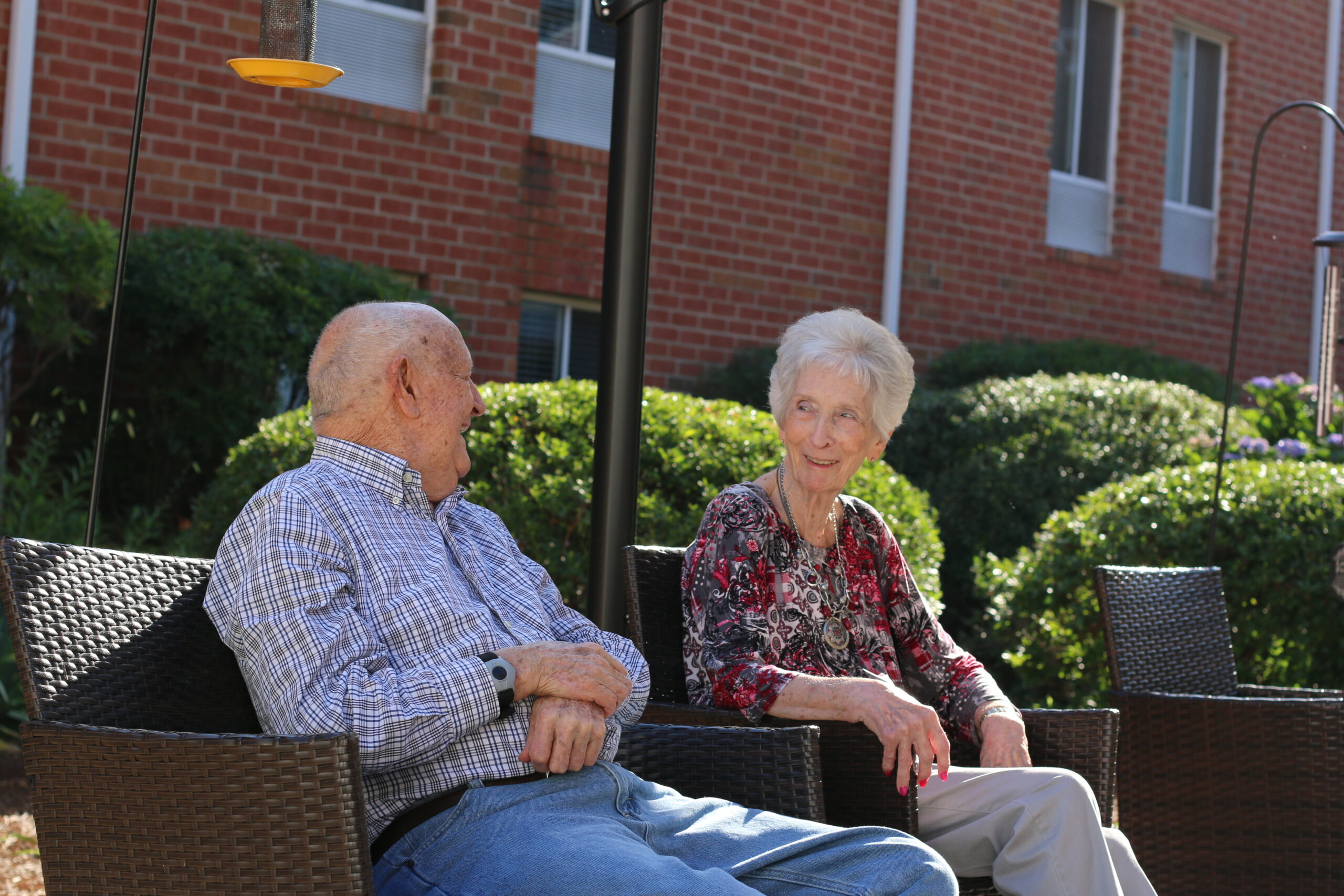 Two senior residents enjoy a conversation while sitting outside in the shade at a Kingston Healthcare community